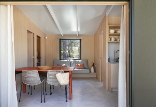 Glamping-accommodatie met houten terras, lichte open ruimte, rotan stoelen en een comfortabele bank.