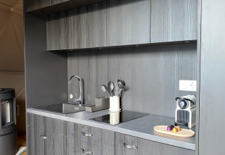 Moderne zwarte kitchenette in de Domo Family-koepel bij Wecamp Pedraforca, Spanje, met koffiemachine en wasbak.