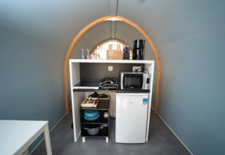 Pequeña cocina en la tienda safari Coco Couple del Weekend Glamping Resort en Italia, con microondas y nevera.