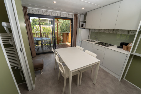 Cocina de lodge moderna con mesa blanca, cuatro sillas y acceso a terraza exterior con árboles.