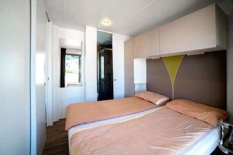Bright modern lodge room with two single beds, overhead cabinets, and shower area in the background.