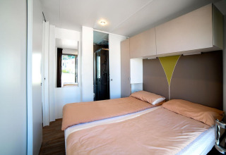 Bright modern lodge room with two single beds, overhead cabinets, and shower area in the background.