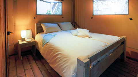 Soveværelse i Safari Lodge telt på Weekend Glamping Resort i Italien med dobbeltseng og hyggelig belysning.