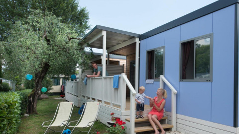 Family relaxing outside their blue Next L Deluxe lodge at Weekend Glamping Resort in Italy, enjoying a sunny day.