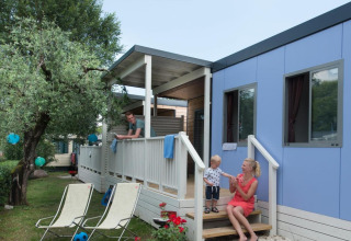 Family relaxing outside their blue Next L Deluxe lodge at Weekend Glamping Resort in Italy, enjoying a sunny day.