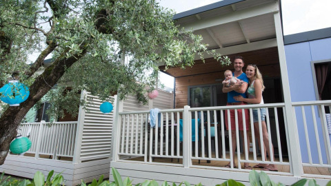 Family on the porch of Next L Deluxe lodge at Weekend Glamping Resort in Italy, with lanterns and trees.