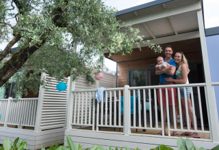 Family on the porch of Next L Deluxe lodge at Weekend Glamping Resort in Italy, with lanterns and trees.