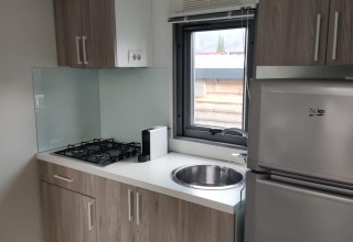 Modern kitchenette at Next L Deluxe Weekend Glamping Resort in Italy with stove, fridge, and window view.