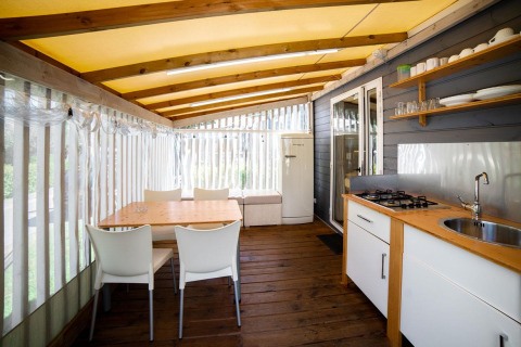 Indbydende glamping Cottage Clever køkken og spiseområde med trægulve, moderne hvide møbler og hyggelig stemning.