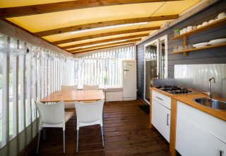 Indbydende glamping Cottage Clever køkken og spiseområde med trægulve, moderne hvide møbler og hyggelig stemning.