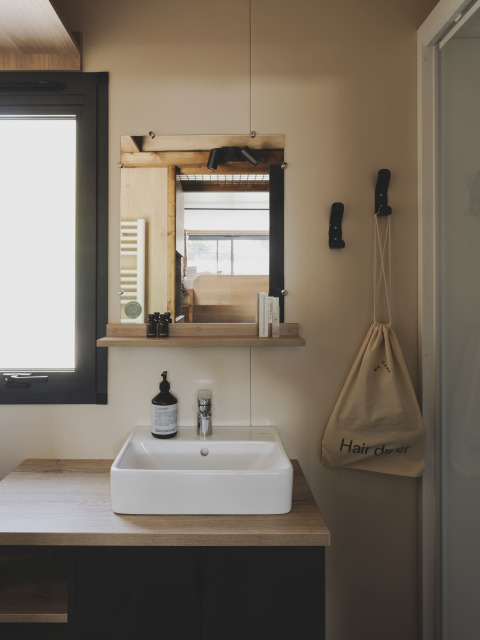 Moderne mini badkamer met wasbak, plank, spiegel en tas in Tiny Home Family bij Wecamp Jávea, Spanje.