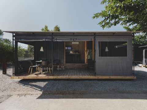 Modern tiny house genaamd TINY HOME FAMILY met overdekt terras en zitgedeelte buiten in het daglicht.