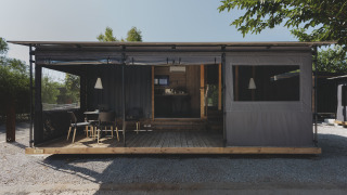 Et moderne tiny house kaldet TINY HOME FAMILY med overdækket terrasse og udendørs siddepladser i solskin.
