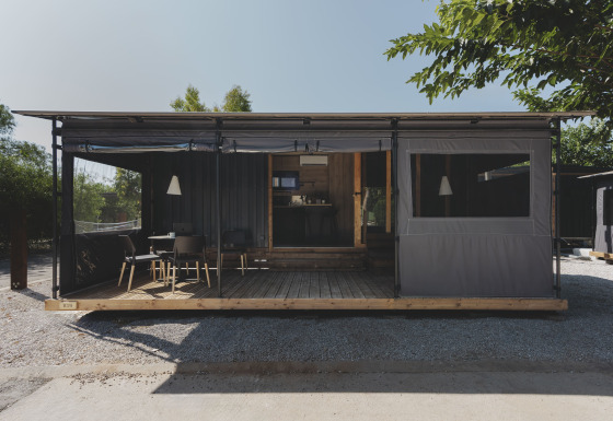 Modern tiny house genaamd TINY HOME FAMILY met overdekt terras en zitgedeelte buiten in het daglicht.