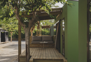 Houten terras bij chalet MOBIL HOME FAMILY op Wecamp Jávea, Spanje, met boom en moderne groene wand.