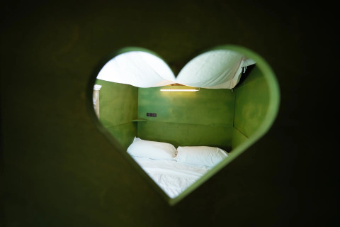 Uitzicht op een knus tweepersoonsbed door een hartvormig raam in een Air Lodge safaritent in Italië.