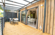 Modern lodge with a wooden deck patio, outdoor dining set, and large glass doors leading inside.