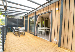 Moderne lodge met houten terras, eettafel buiten en grote glazen schuifdeuren naar de woonkamer.