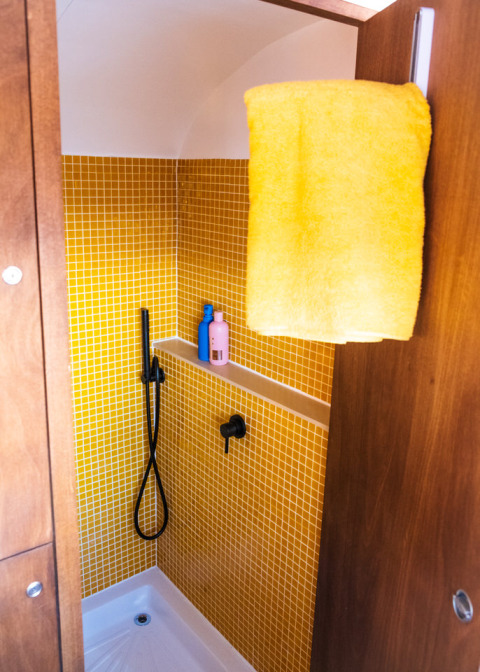 Moderne douche met gele tegels en handdoek bij Airstream tiny house in Chianti Glamping Resort, Italië.