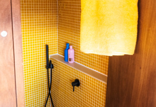 Moderne douche met gele tegels en handdoek bij Airstream tiny house in Chianti Glamping Resort, Italië.