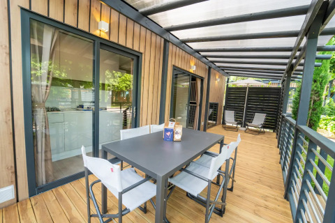Overdækket træterrasse ved glamping-indkvartering med spisebord, stole og afslapningsområde udenfor.