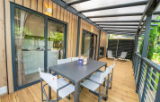 Covered wooden terrace at a glamping accommodation with dining table, chairs, and outdoor lounging area.