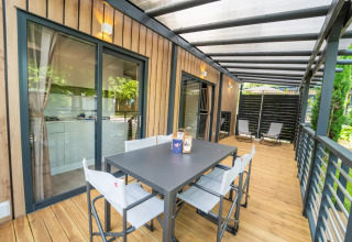Terrasse en bois couverte d’un hébergement glamping avec table à manger, chaises et coin détente extérieur.