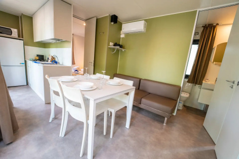 Moderne glamping accommodatie met keukentje, eettafel, zetel en badkamer met groene muren.