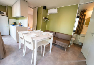 Alojamiento de glamping moderno con cocina, mesa de comedor, sofá y baño en tonos verdes.