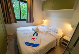 Chambre glamping confortable avec lit double, fenêtre sur la nature, serviettes et lampes murales.