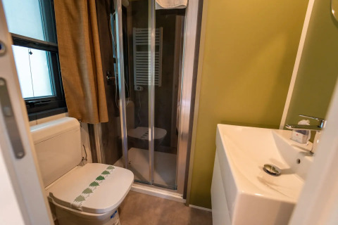 Salle de bain confortable dans un hébergement glamping, avec WC, douche, fenêtre et lavabo blanc.