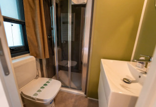 Gezellige badkamer bij glampingverblijf met toilet, douche, raam met gordijn en moderne wastafel.