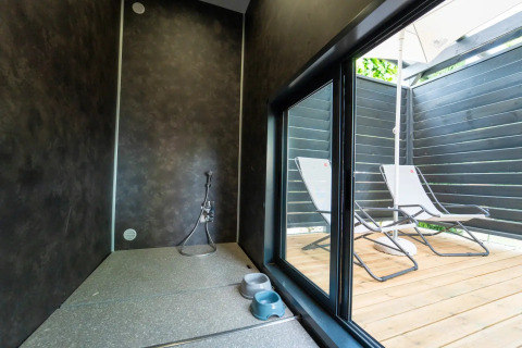 Et moderne glamping-ophold med et udendørs afslapningsområde, liggestole og et indendørs bruseområde.