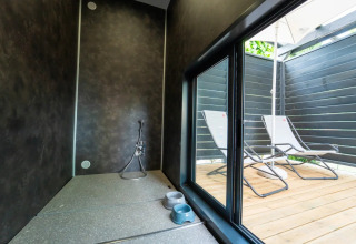 Moderne glamping met binnenruimte voor huisdieren en een terras buiten met ligstoelen en parasol.