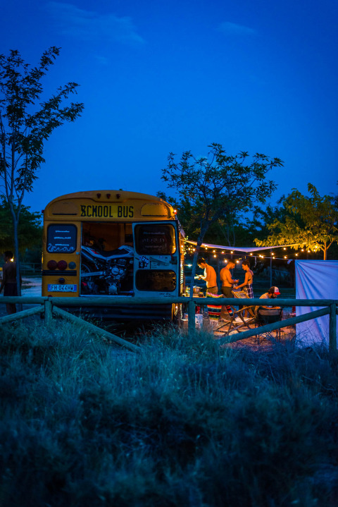 Un ancien bus scolaire au Chianti Glamping Resort en Italie, des gens campent sous guirlandes lumineuses.