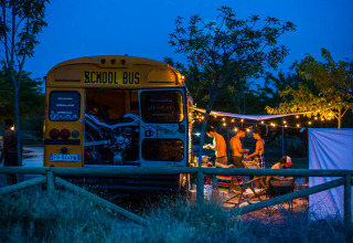 Un ancien bus scolaire au Chianti Glamping Resort en Italie, des gens campent sous guirlandes lumineuses.