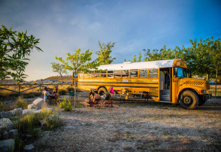 Tiny house dans un ancien bus scolaire au Chianti Glamping Resort, Italie, avec des invités assis en plein air.