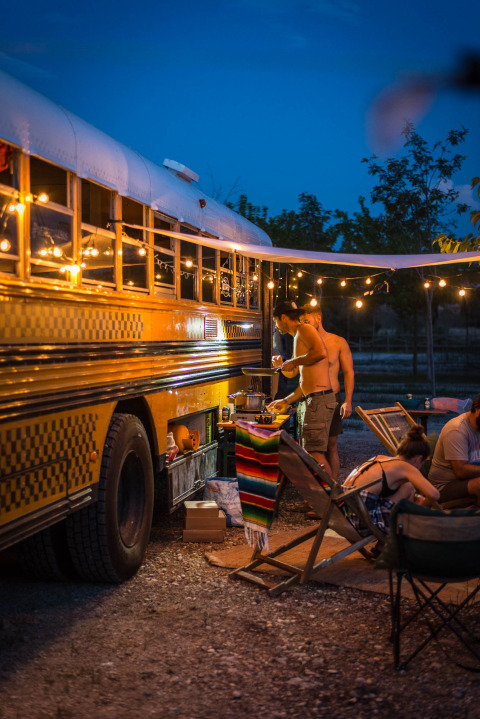Ambiance nocturne conviviale près d’un bus scolaire aménagé au Chianti Glamping Resort en Italie avec guirlandes lumineuses.