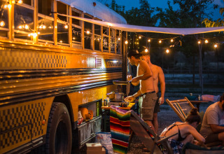Ambiance nocturne conviviale près d’un bus scolaire aménagé au Chianti Glamping Resort en Italie avec guirlandes lumineuses.