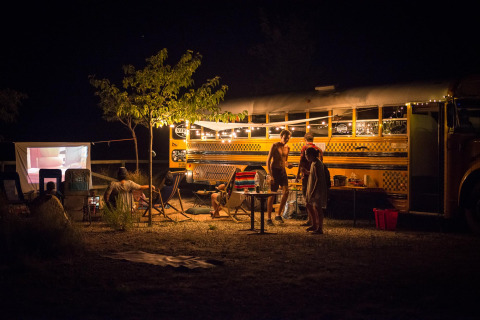 Scène nocturne de personnes campant près d’un tiny house bus à Chianti Glamping Resort en Italie.