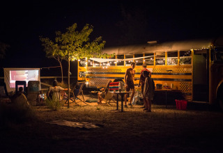 Scène nocturne de personnes campant près d’un tiny house bus à Chianti Glamping Resort en Italie.