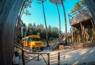 Photo d’un bus scolaire jaune transformé en tiny house au Chianti Glamping Resort, en Italie, entouré d’arbres.