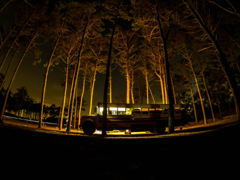Un tiny house en bus scolaire éclairé dans une forêt la nuit au Chianti Glamping Resort en Italie.