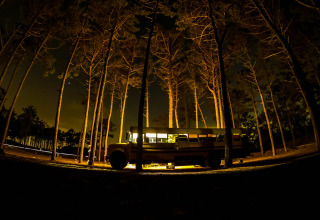 Un tiny house en bus scolaire éclairé dans une forêt la nuit au Chianti Glamping Resort en Italie.