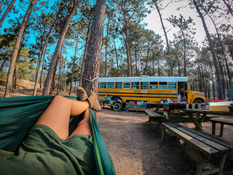 Personne se relaxant dans un hamac près d'une tiny house bus scolaire dans la forêt au Chianti Glamping Resort, Italie.