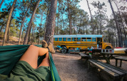 Person entspannt in einer Hängematte neben einem Schulbus-Tiny-House im Wald beim Chianti Glamping Resort, Italien.