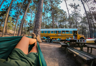 Personne se relaxant dans un hamac près d'une tiny house bus scolaire dans la forêt au Chianti Glamping Resort, Italie.