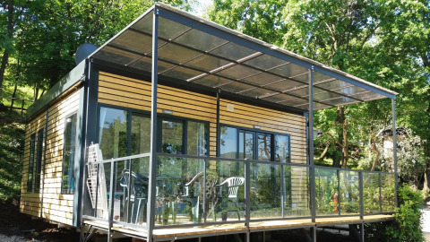 Lodge Next XL Panorama avec véranda moderne en verre, façade en bois et arbres verdoyants autour.