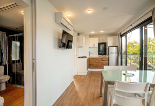 Intérieur de lodge lumineux avec cuisine moderne, salon, table à manger et vue sur la nature par de grandes fenêtres.