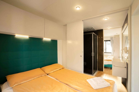 Chambre moderne avec lit double, draps jaunes et salle de bain attenante, Next XL Panorama, Chianti Glamping Resort.